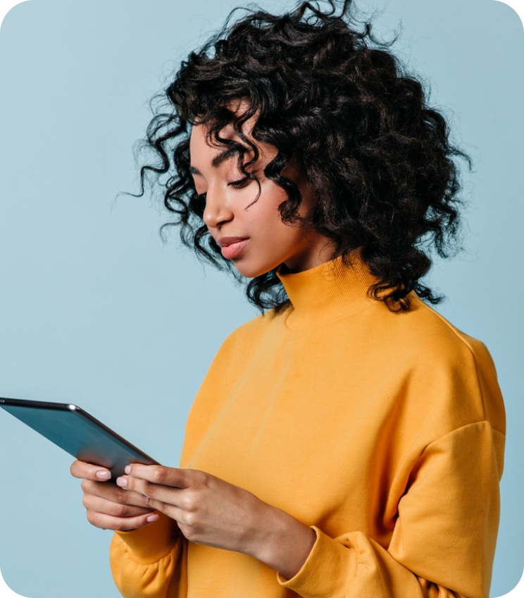 Woman wearing a yellow sweater using a tablet against a blue background.